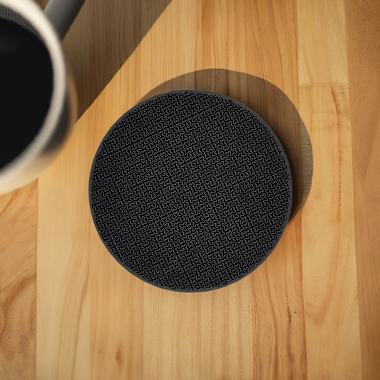 AI generated image of a black H curve pattern infill coaster on a light wood surface next to a coffee cup