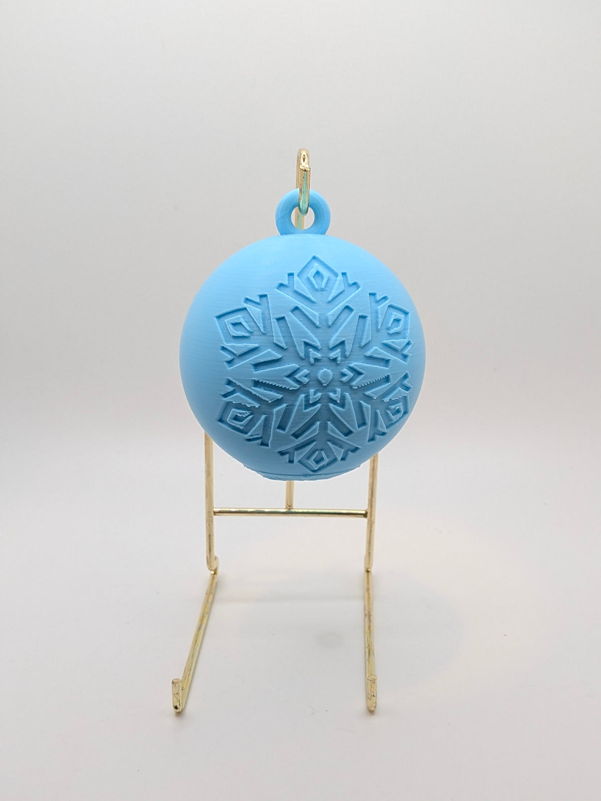 aqua bauble with snowflake pattern on a stand against a white background