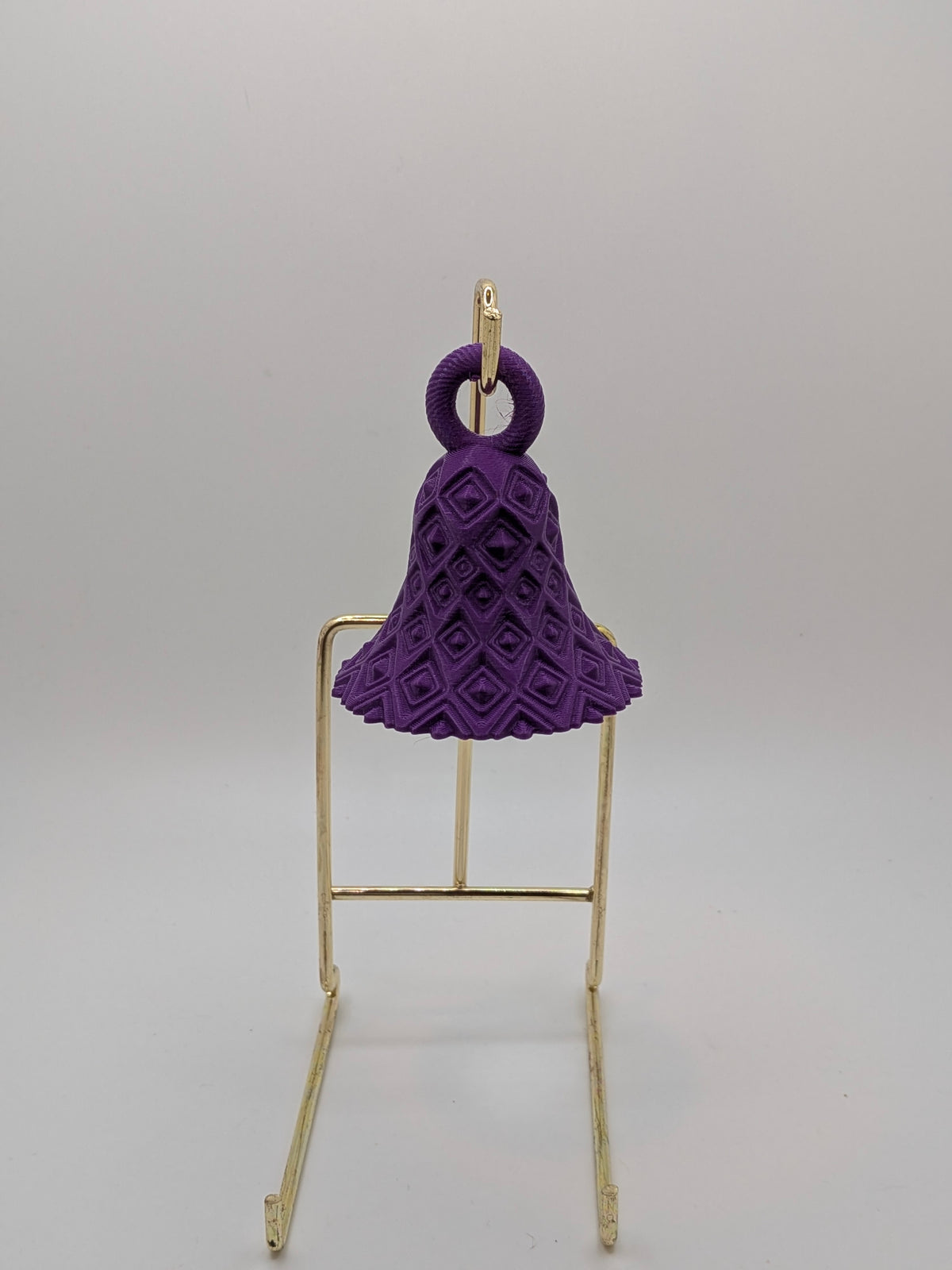 Purple textured bell-shaped object on a gold stand against a gray background